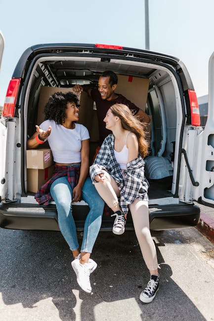 Two movers from Man with Van Battersea are engaged in a home relocation process, loading a large, dark green piece of furniture into the open rear of a white van parked on a street. The interior of th
